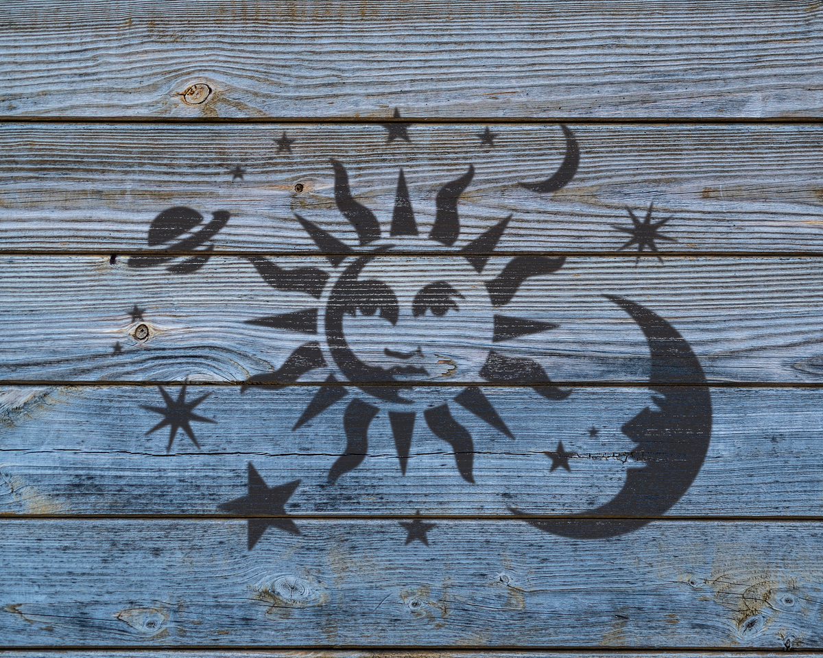a wooden surface with a black sun and moon stencil, along with various stars and other celestial elements.
