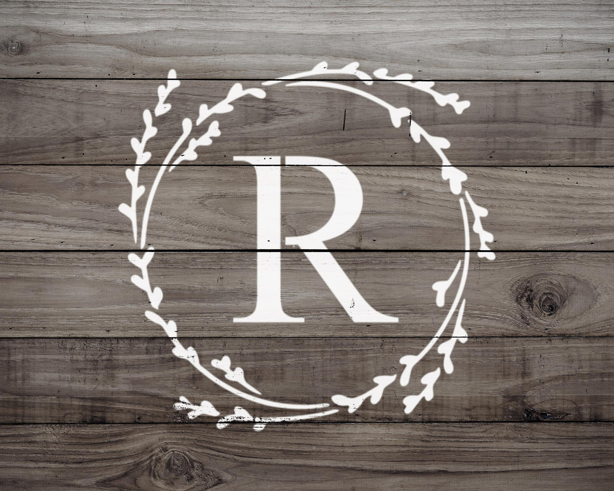 A monogrammed letter "R" in the center of a wreath-like design on a wooden background.