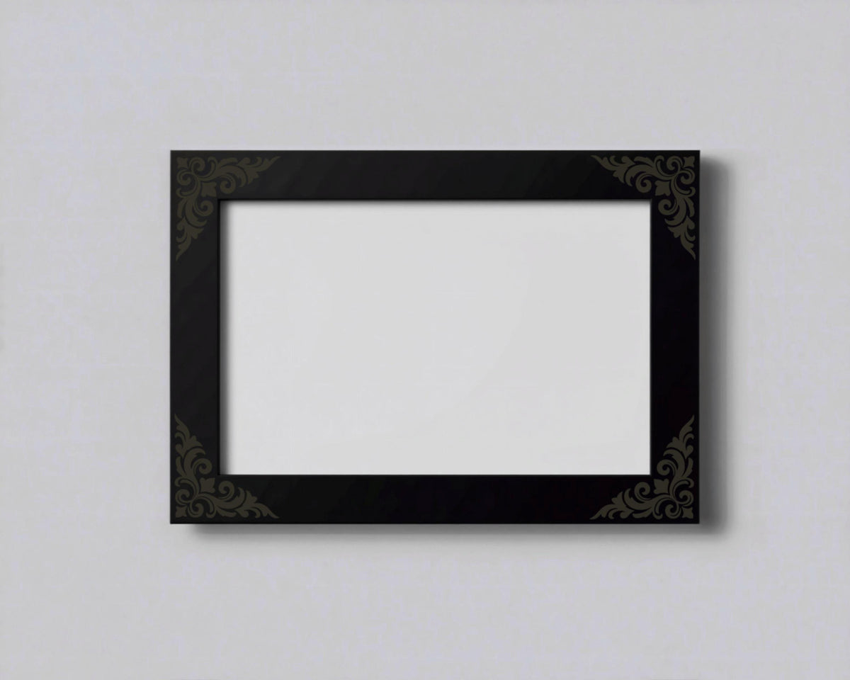 A black picture frame with a decorative border is hanging on a plain white wall.