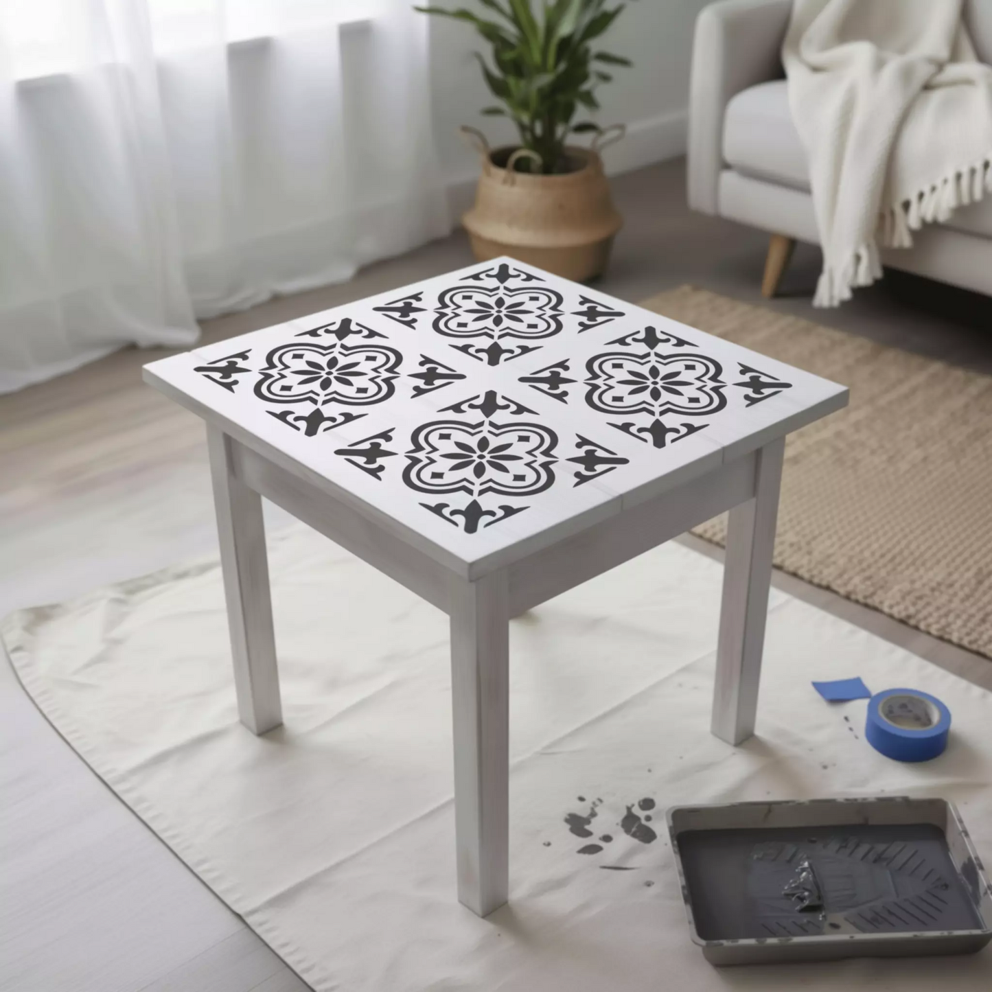 a white table with a decorative tile design on its surface, placed on a white cloth on a wooden floor. In the background, there is a couch and a potted plant, creating a cozy and inviting atmosphere.