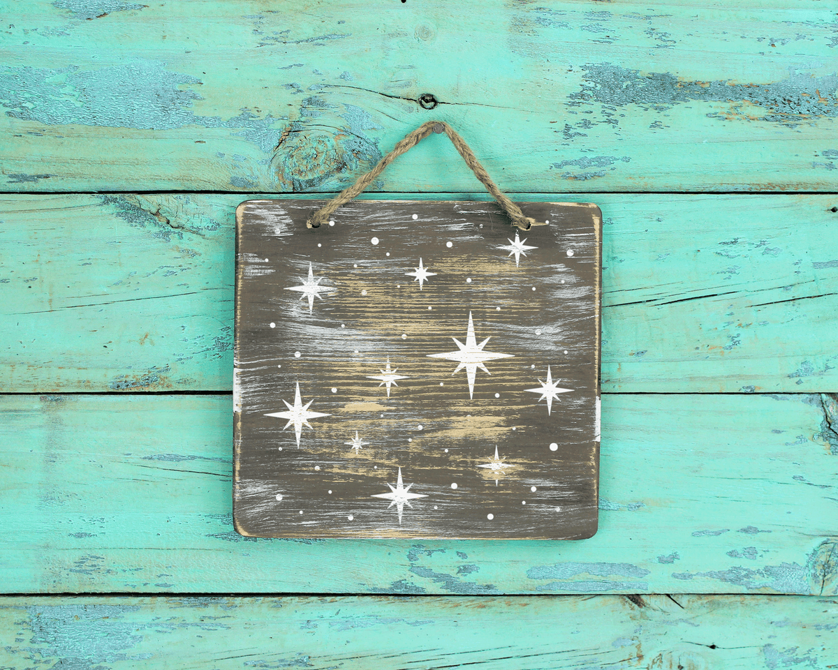 A weathered wooden sign with a starry night sky design is hanging on a turquoise wooden surface.
