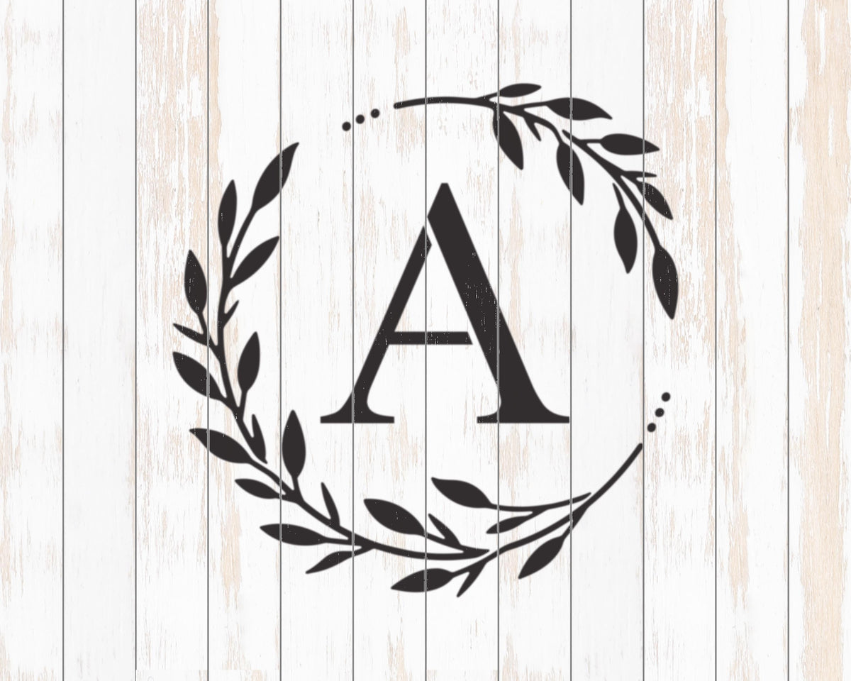 A monogrammed letter "A" surrounded by a wreath of leaves and branches against a white wooden background.