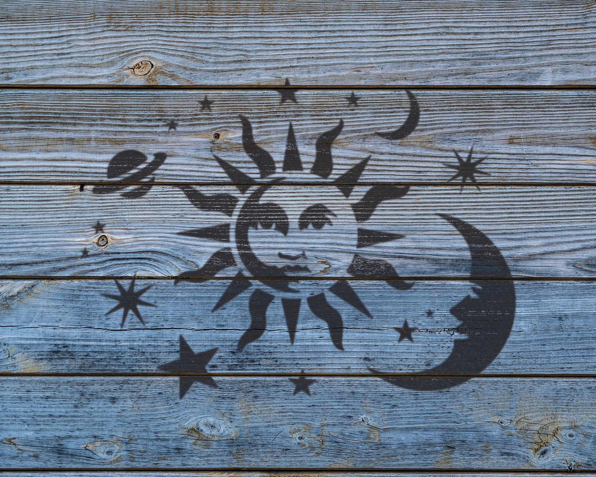 a wooden surface with a black sun and moon stencil, along with various stars and other celestial elements.