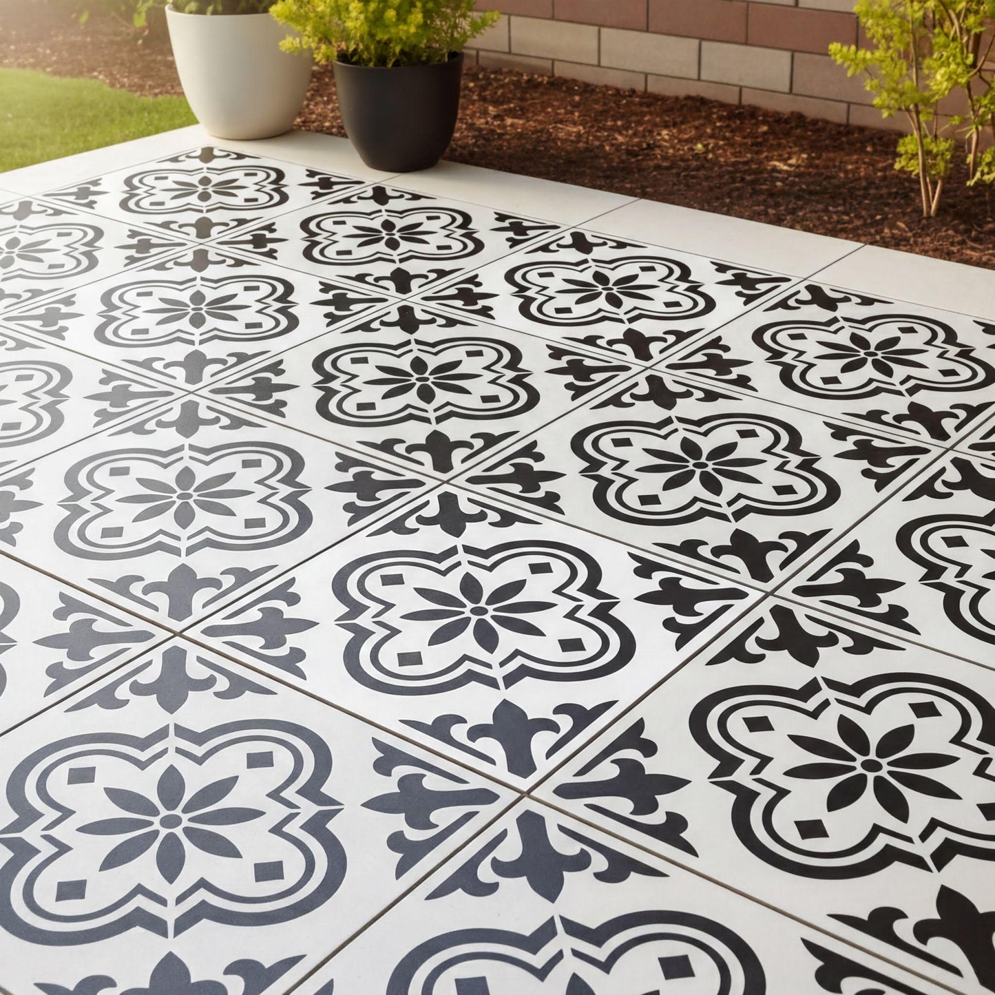 a tiled floor with a black and white pattern, including floral and geometric designs. The floor is surrounded by a brick wall and has some plants placed around it.