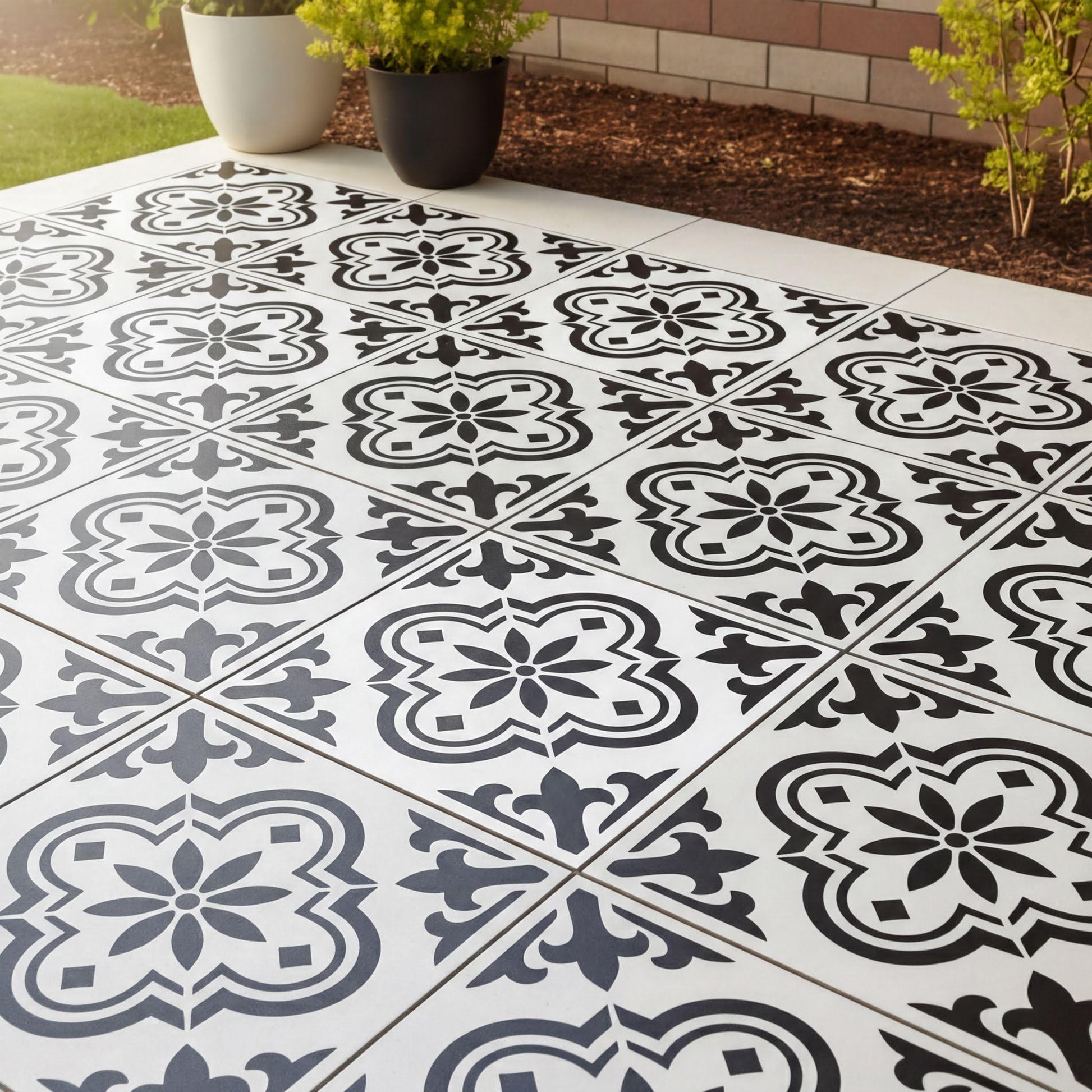 a tiled floor with a black and white pattern, including floral and geometric designs. The floor is surrounded by a brick wall and has some plants placed around it.
