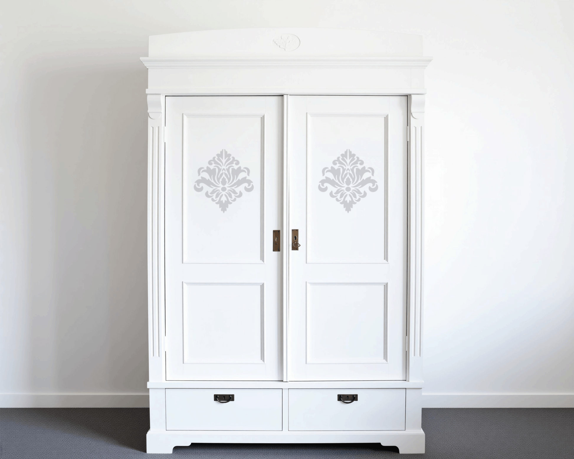 A white wooden wardrobe with two doors and decorative patterns on them, standing against a white wall.