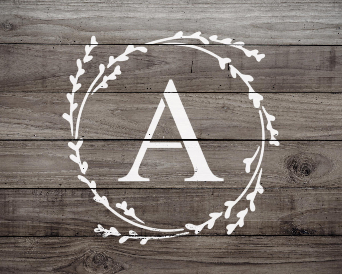 A monogrammed letter "A" in the center of a wreath-like design on a wooden background.