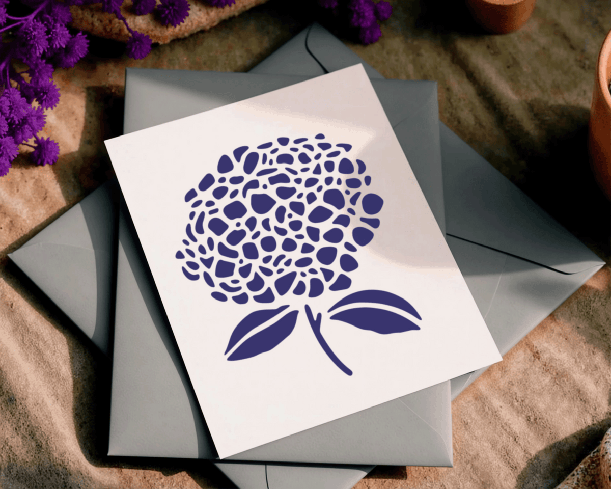 A white card with a blue floral design is placed on top of two gray envelopes, with purple flowers visible in the background.