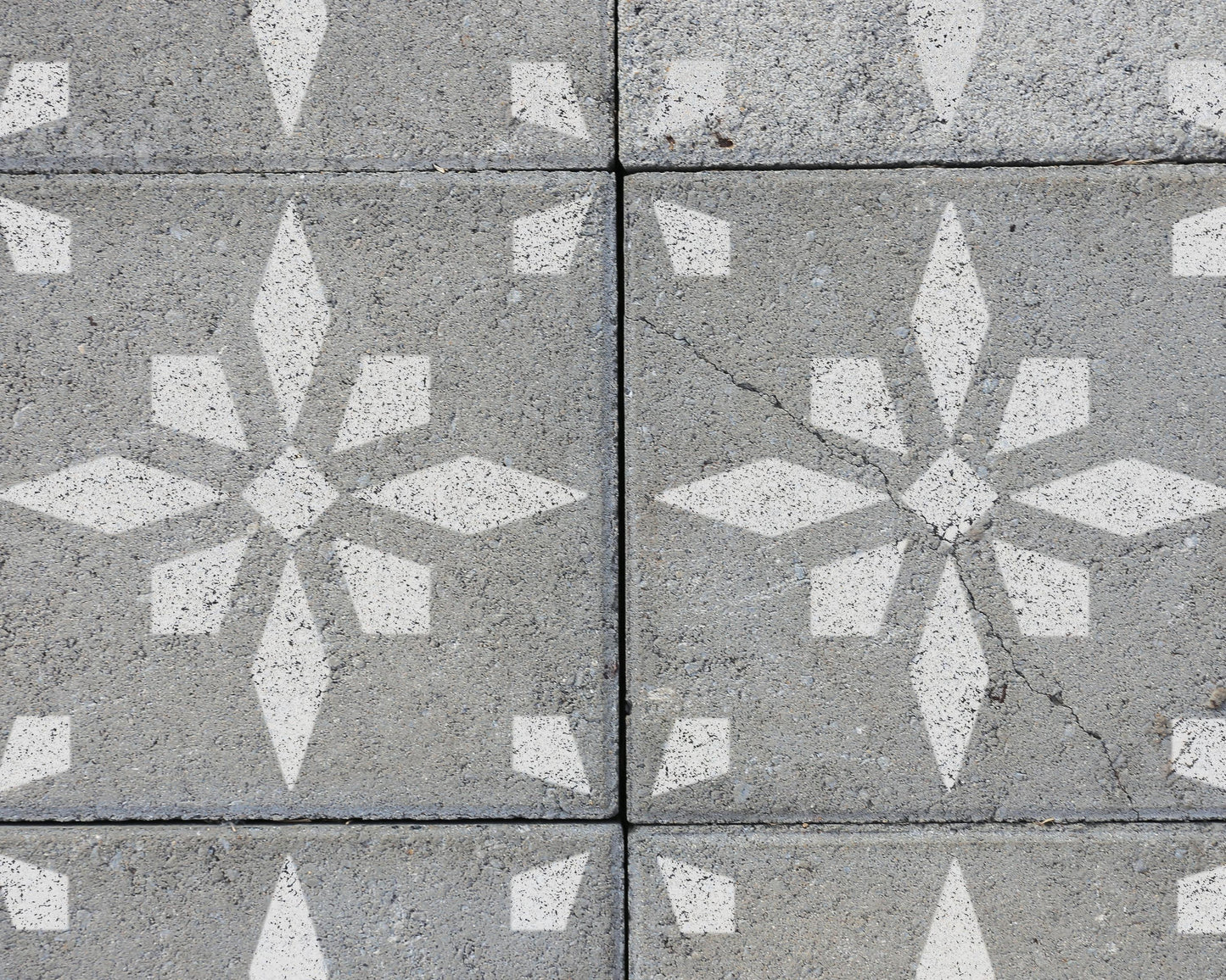 a close-up view of a concrete surface with a repeating pattern of white star-shaped designs. The pattern is composed of multiple white stars arranged in a grid-like fashion, creating a visually striking and symmetrical design.