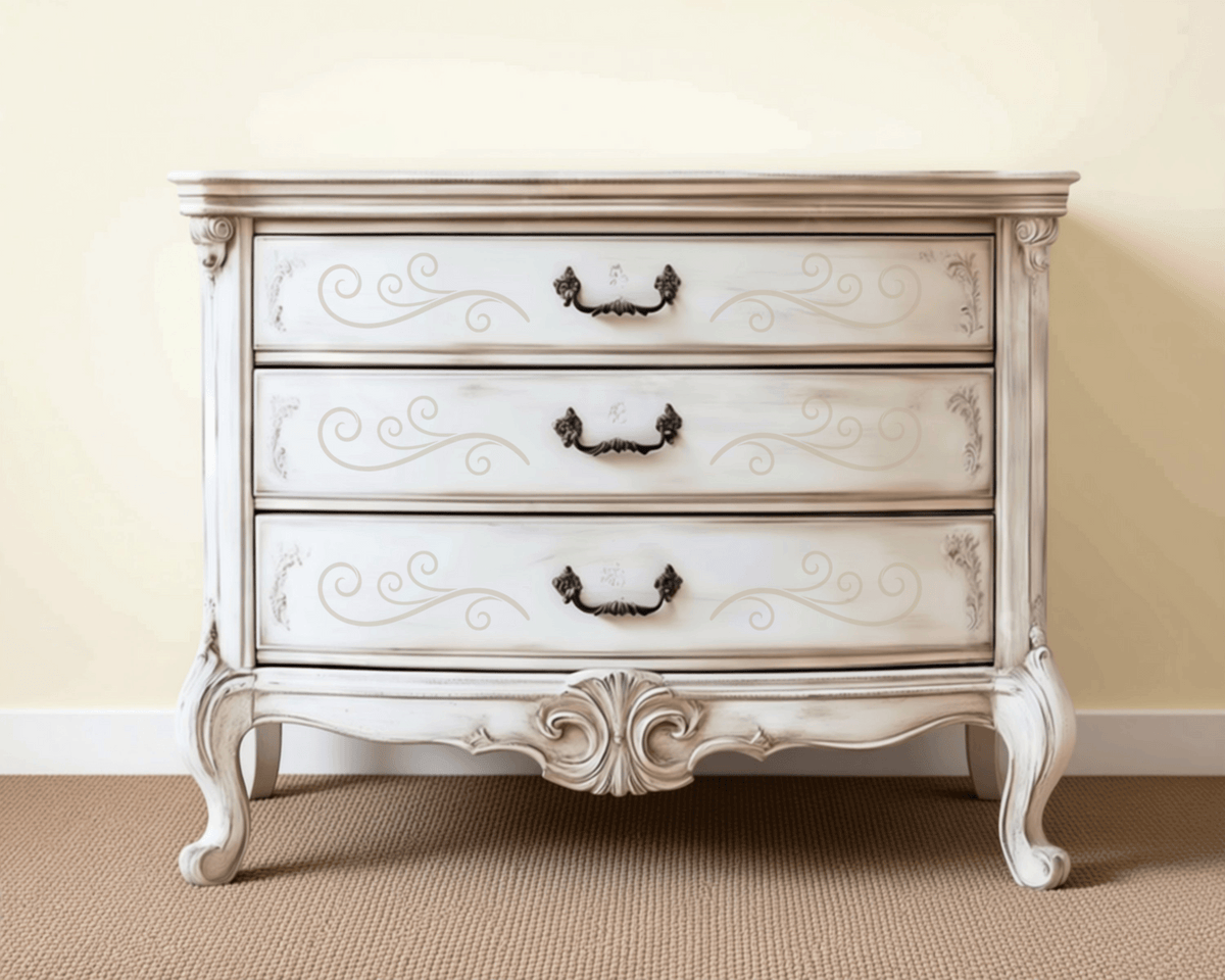A white wooden dresser with three drawers, featuring an ornate, decorative design on the front.