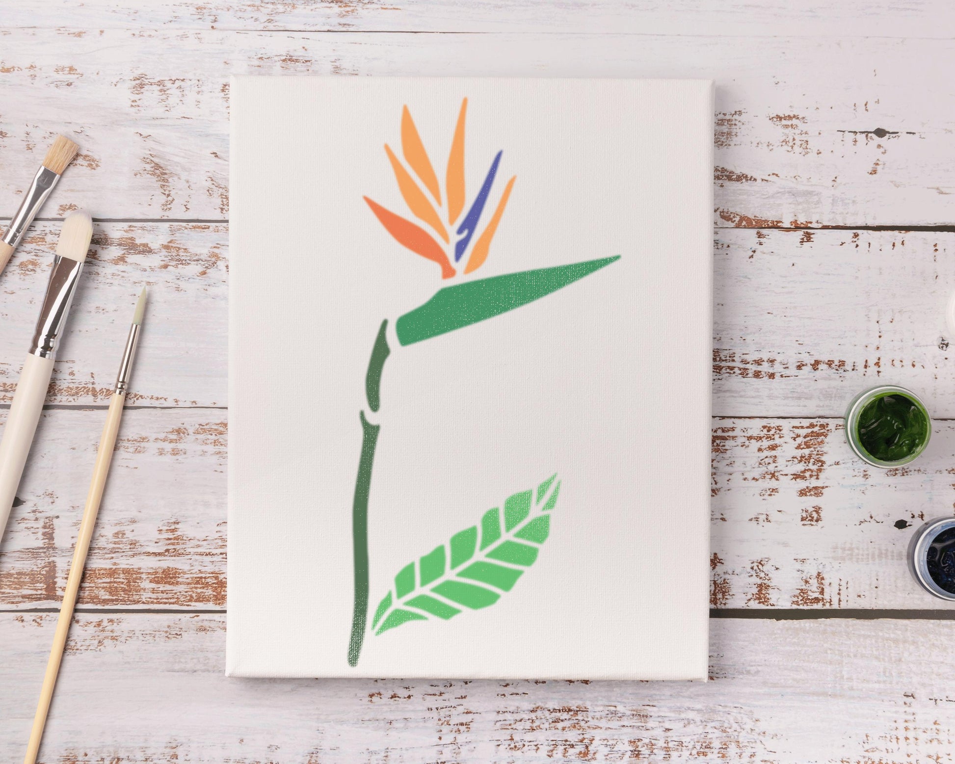 a white canvas with a colorful, stylized flower design on it, along with some art supplies and a wooden surface.