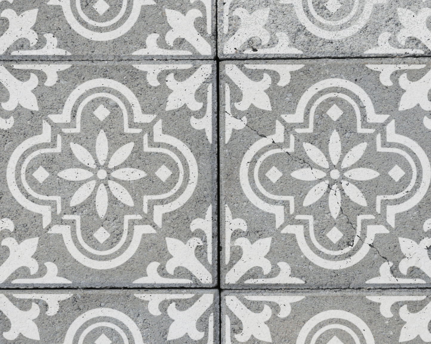 a close-up view of a patterned tile surface, featuring a repeating design of white floral motifs on a gray background.