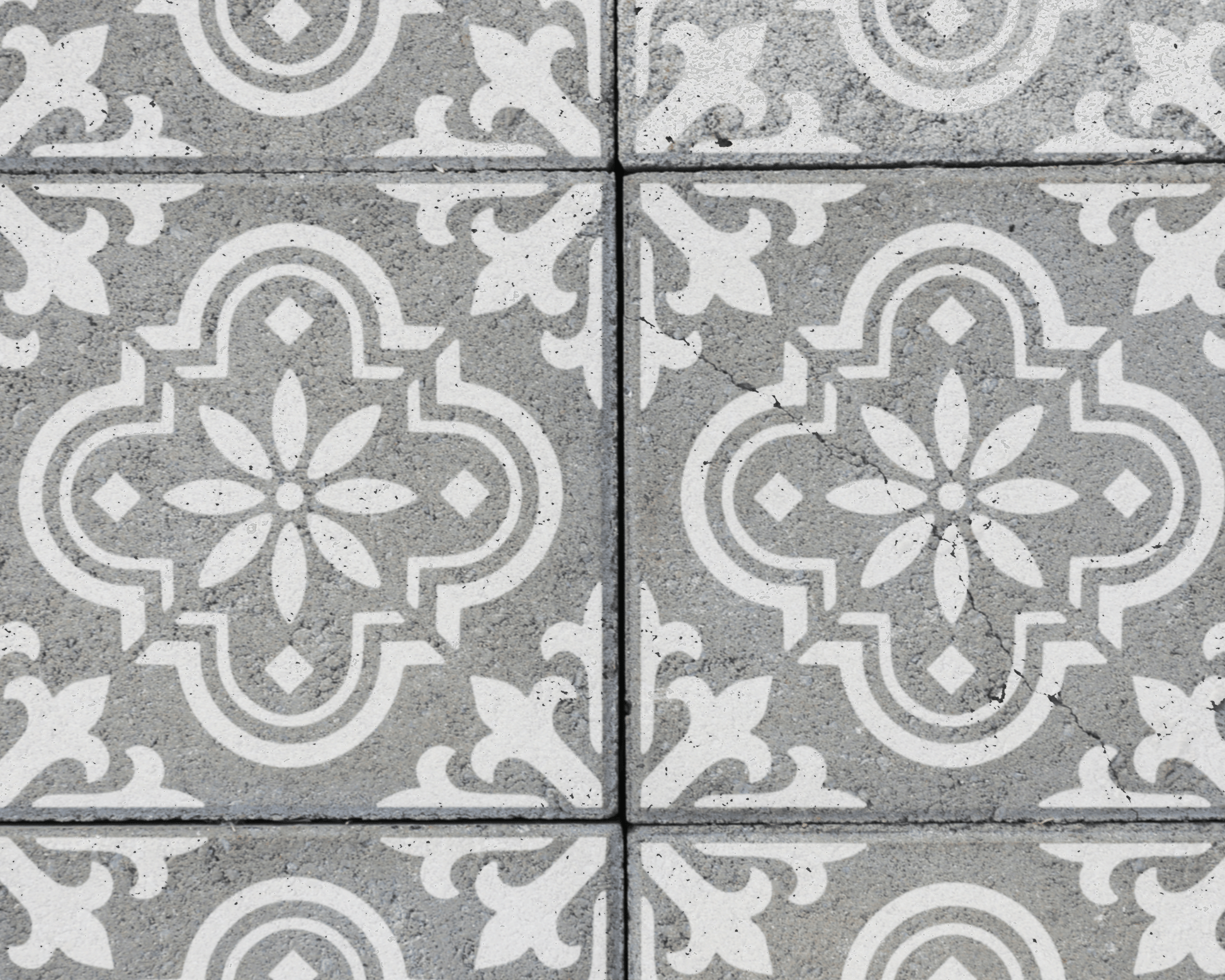 a close-up view of a patterned tile surface, featuring a repeating design of white floral motifs on a gray background.