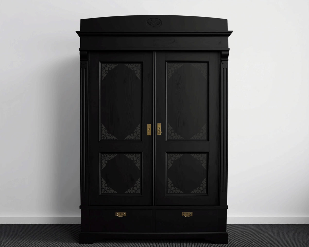 A tall, black wooden wardrobe with ornate designs on the doors and drawers, standing against a white wall.