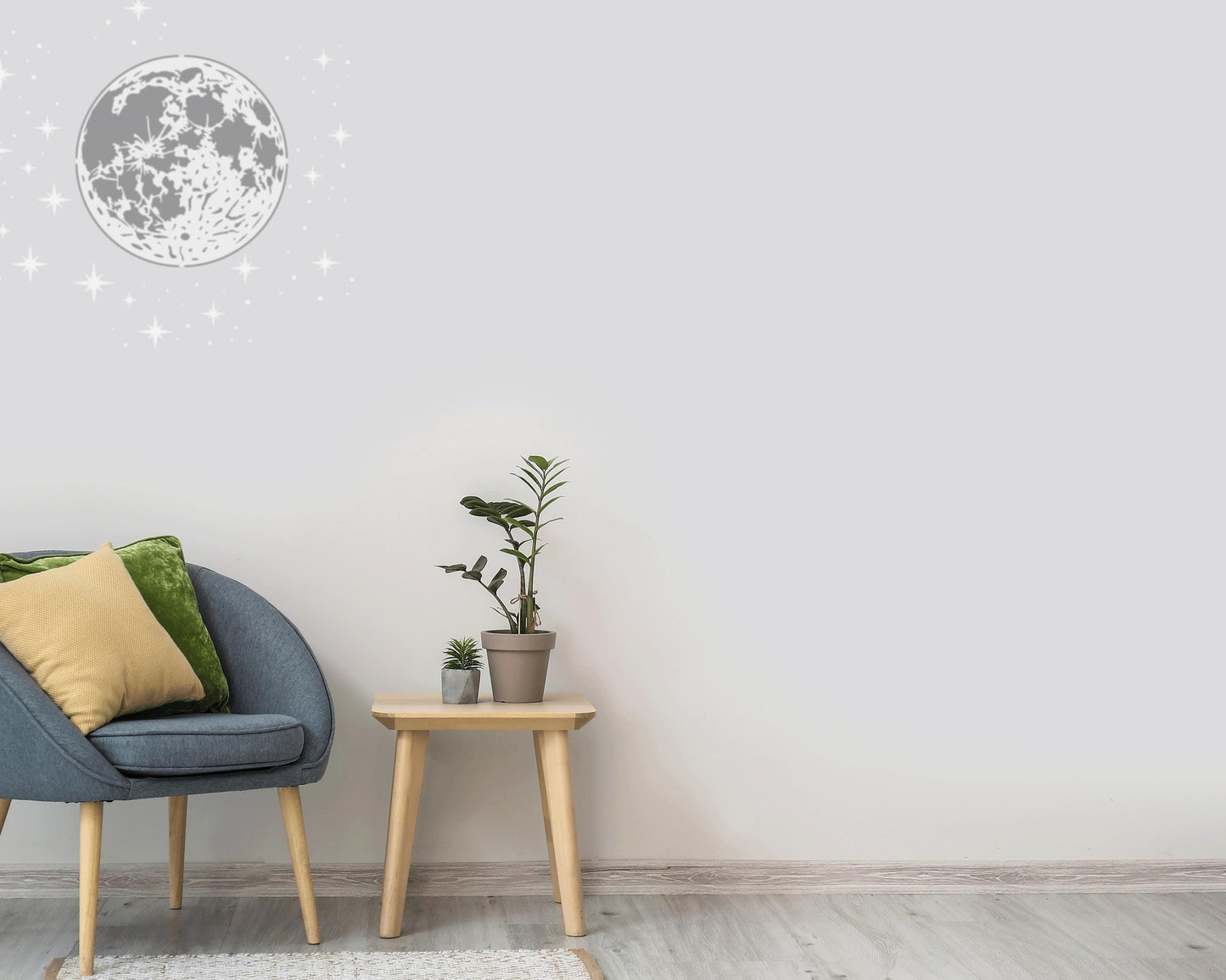 a cozy living room with a gray armchair, a small wooden side table, and a potted plant. The room has a minimalist and modern design, with a large moon-shaped decoration on the wall and a starry background.