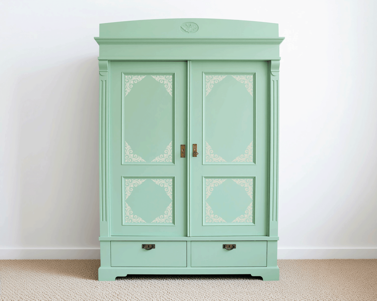 A mint green antique-style wardrobe with decorative patterns on the doors and drawers stands against a white wall.