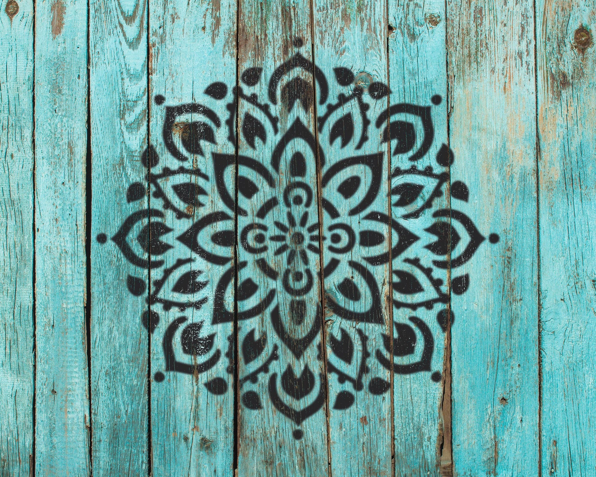a large, intricate mandala design painted on a weathered, turquoise wooden surface.