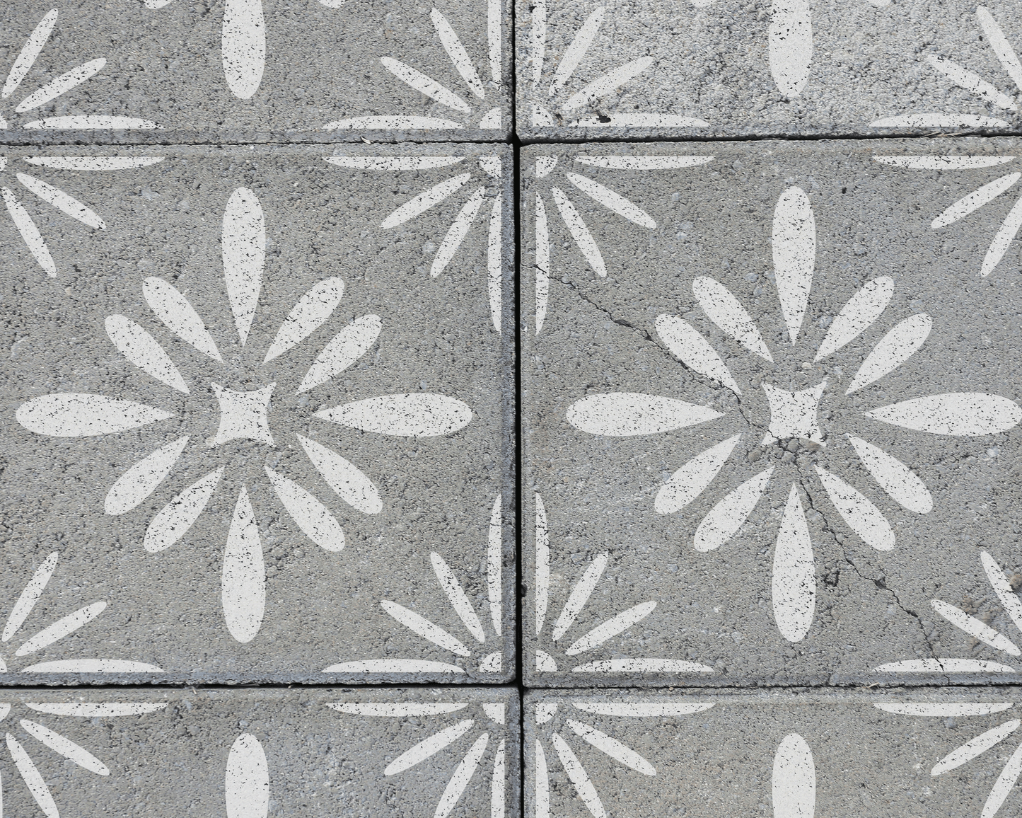 a close-up view of a concrete surface with a repeating pattern of white flower-like designs. The pattern is composed of various shapes and sizes, creating a visually interesting and intricate design.