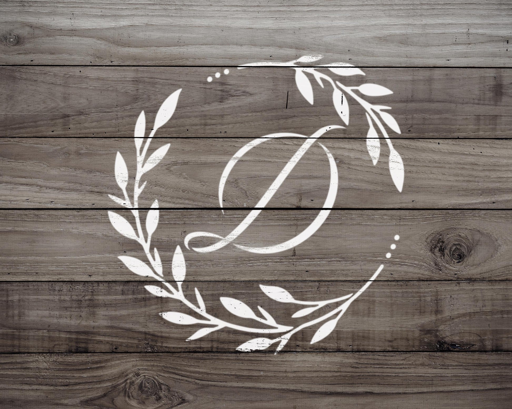 A monogrammed white letter "D" is centered on a wooden background with a wreath of leaves and branches surrounding it.
