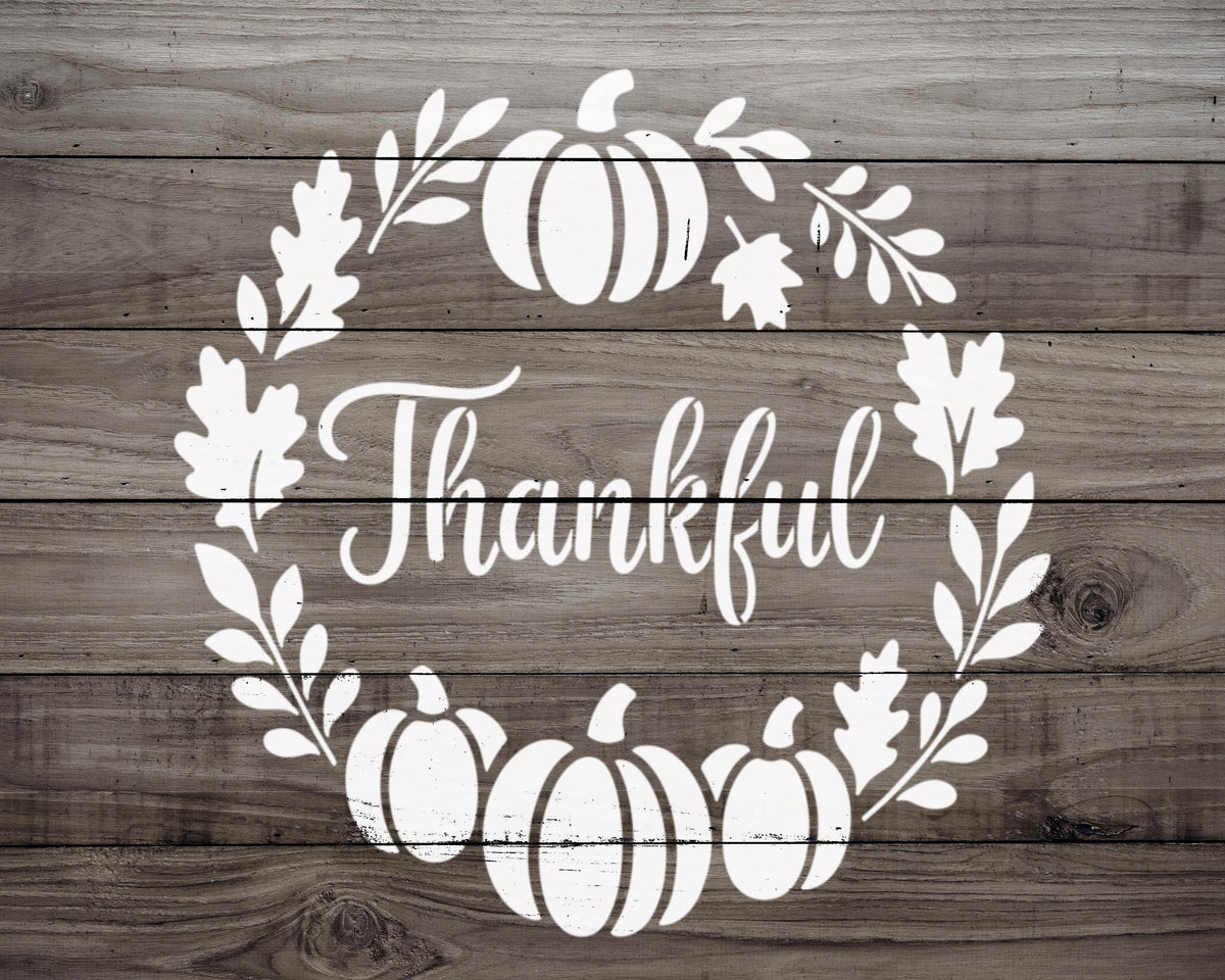 A wreath made of white leaves and pumpkins surrounds the word "Thankful" in a wooden background.