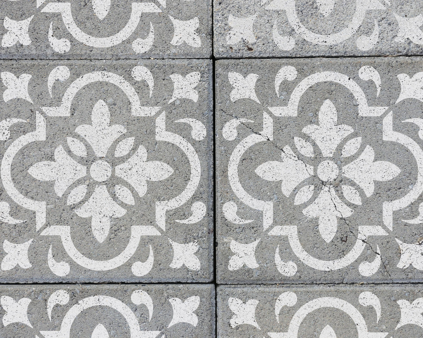 a close-up view of a patterned concrete surface with a repeating design of white floral motifs.