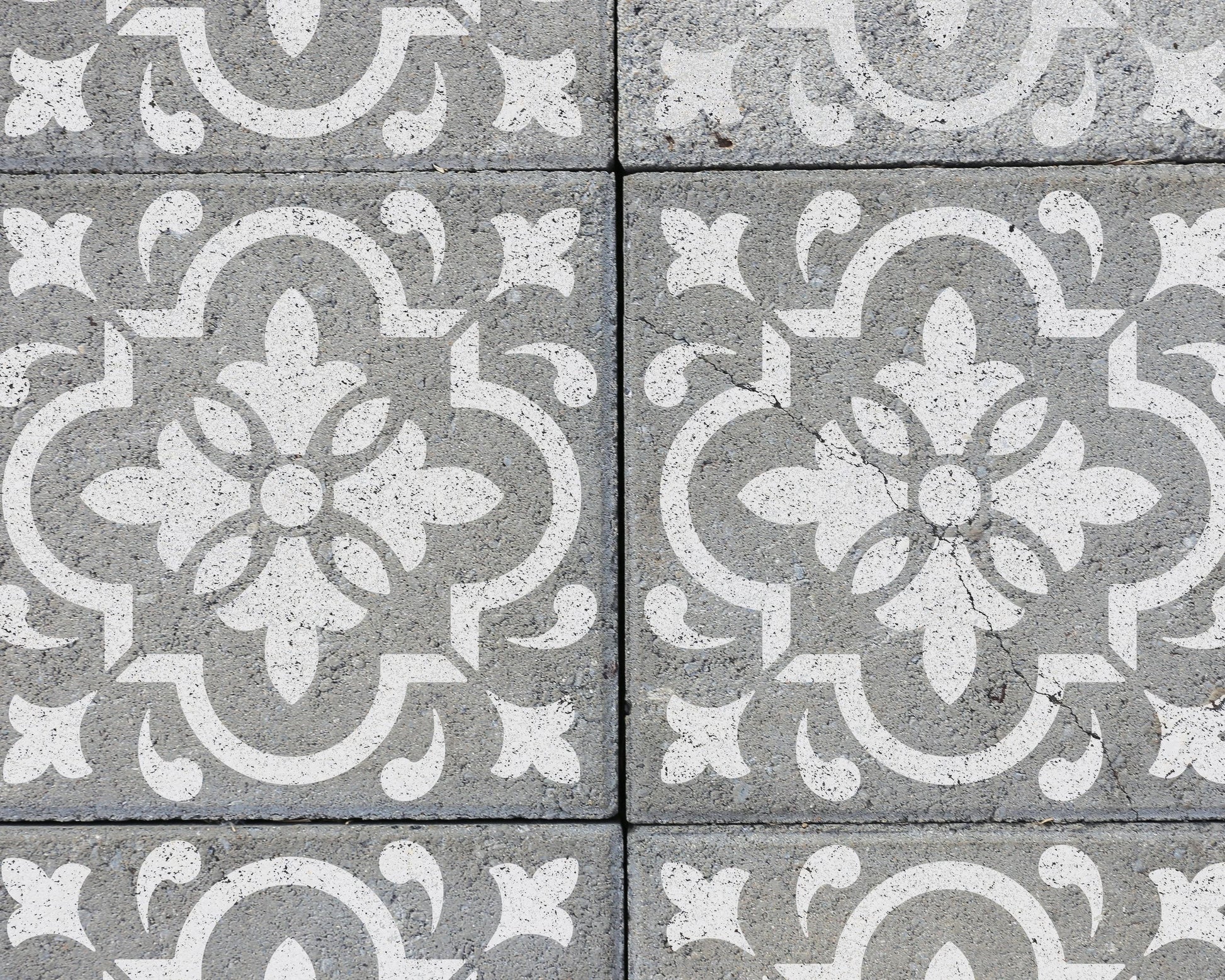 a close-up view of a patterned concrete surface with a repeating design of white floral motifs.