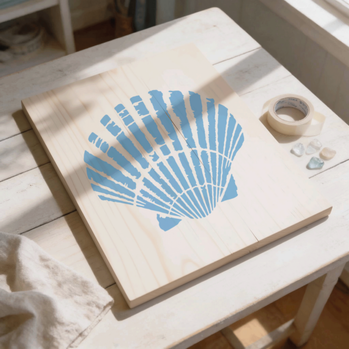A wooden board with a blue shell design is placed on a white table, accompanied by some tape and small stones.