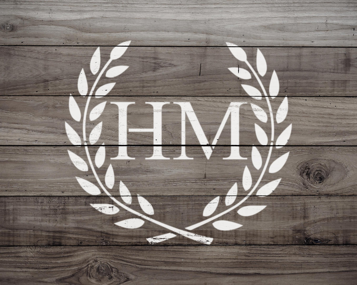 a monogrammed logo consisting of the letters "HMM" surrounded by a laurel wreath design on a wooden background.