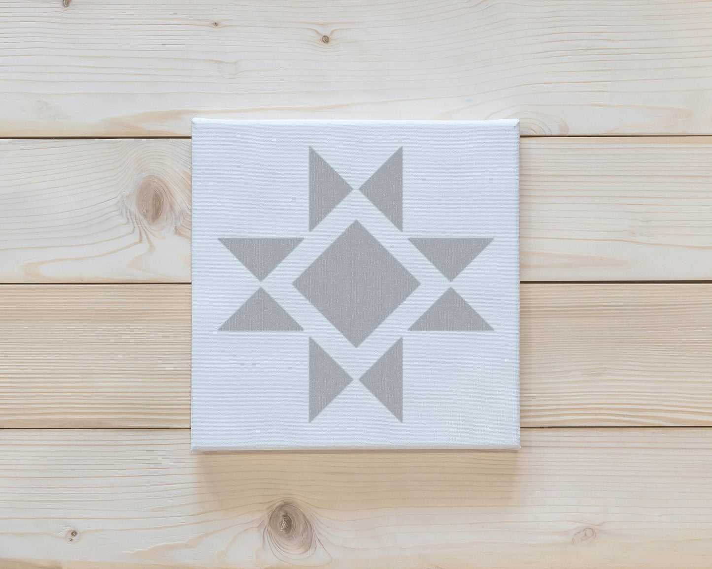 a white canvas with a gray geometric design on it, placed on a wooden surface.