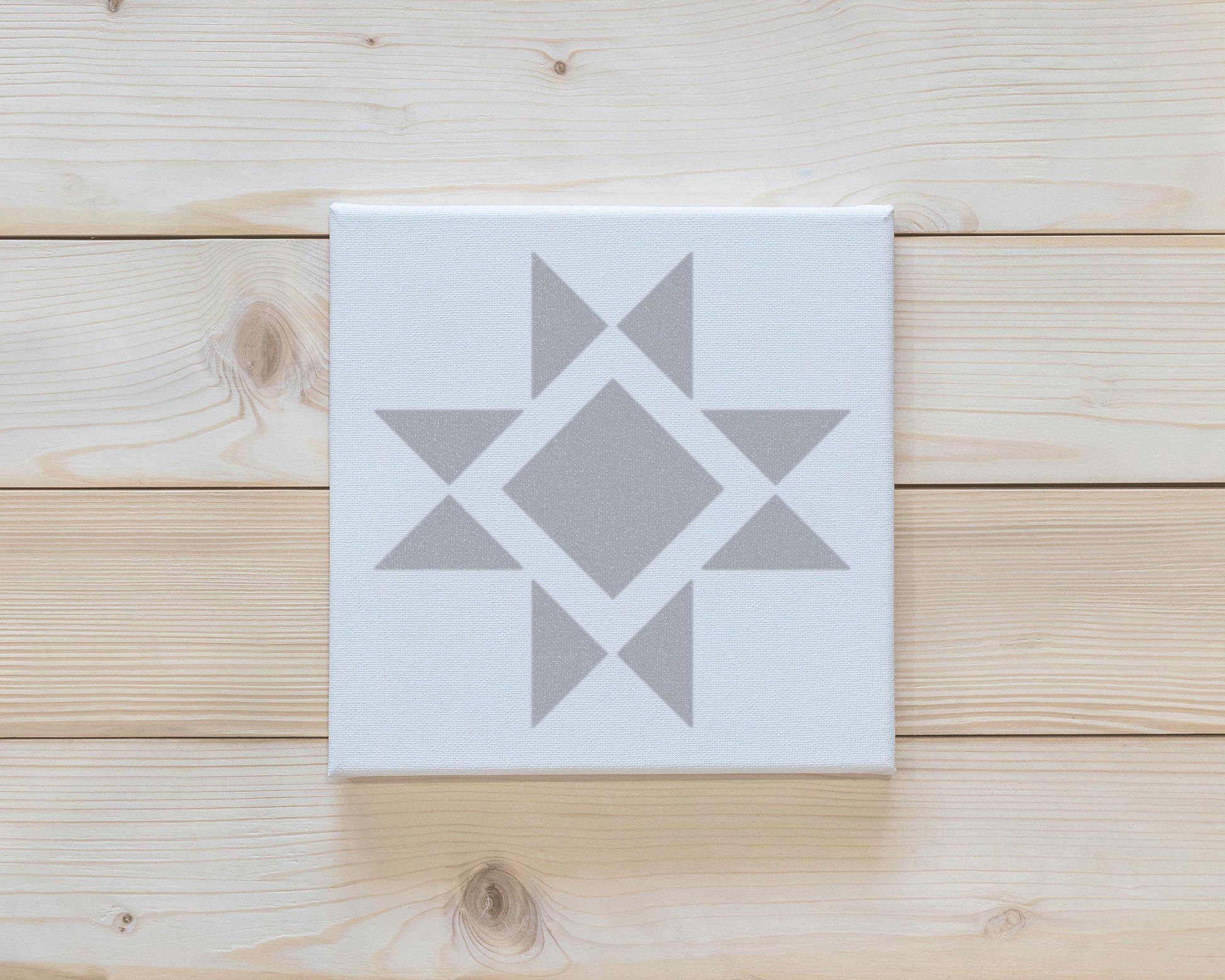 a white canvas with a gray geometric design on it, placed on a wooden surface.