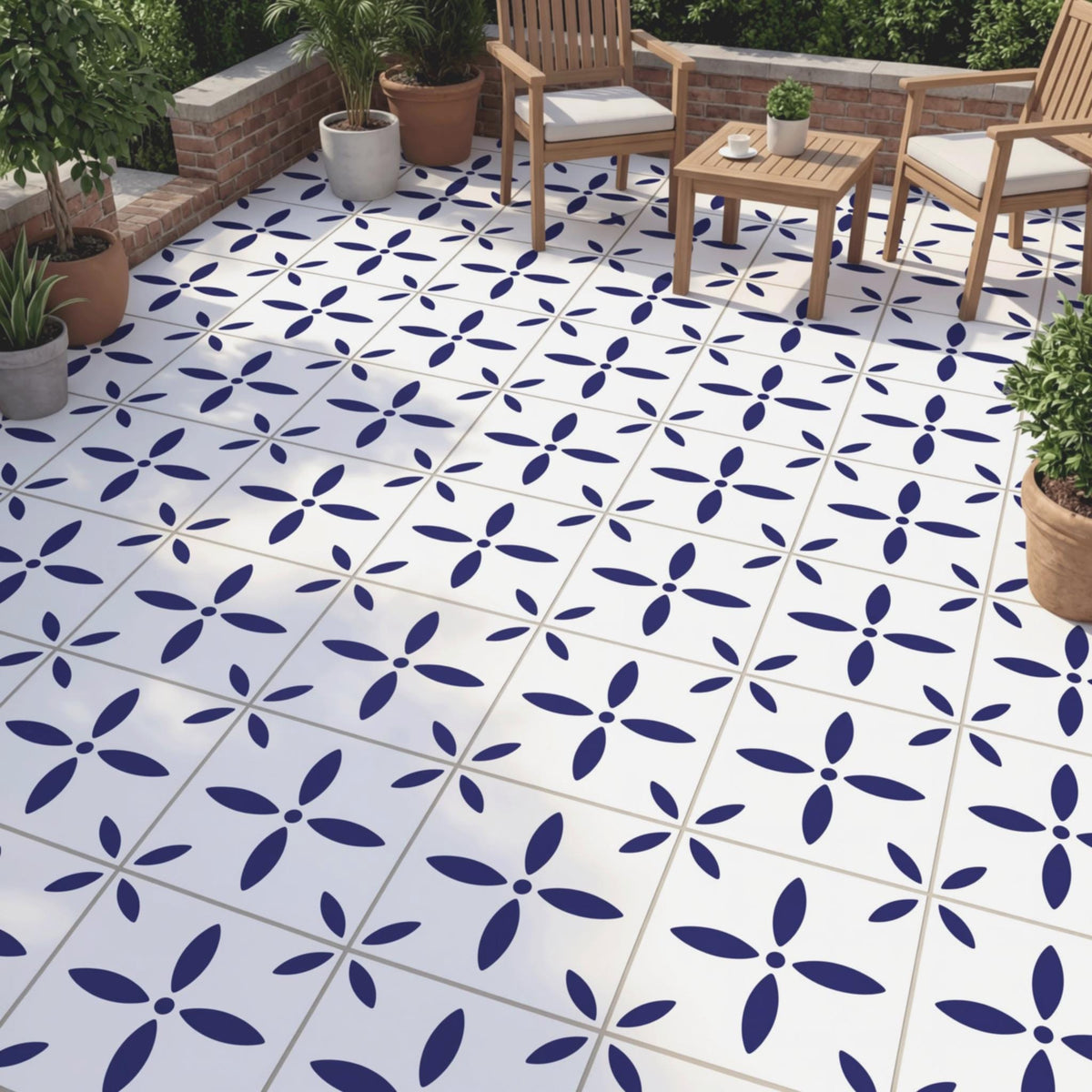 a patio area with a white tile floor adorned with blue flower-like patterns. There are two wooden chairs and a small table placed on the patio, creating a cozy outdoor seating area. The patio is surrounded by potted plants, adding a touch of greenery to the space.