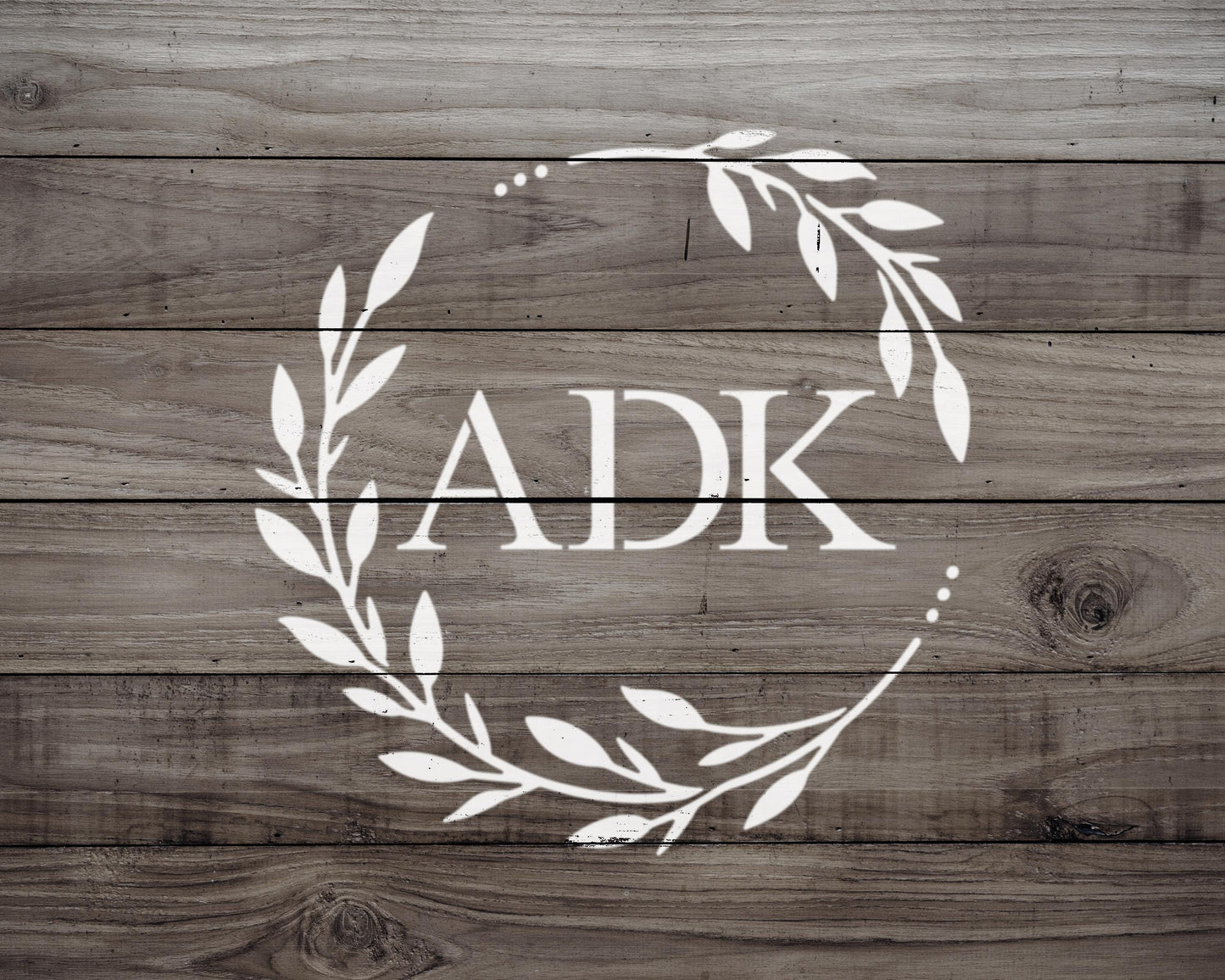 a monogrammed logo with the letters "AK" in the center, surrounded by a wreath-like design made up of leaves and branches.