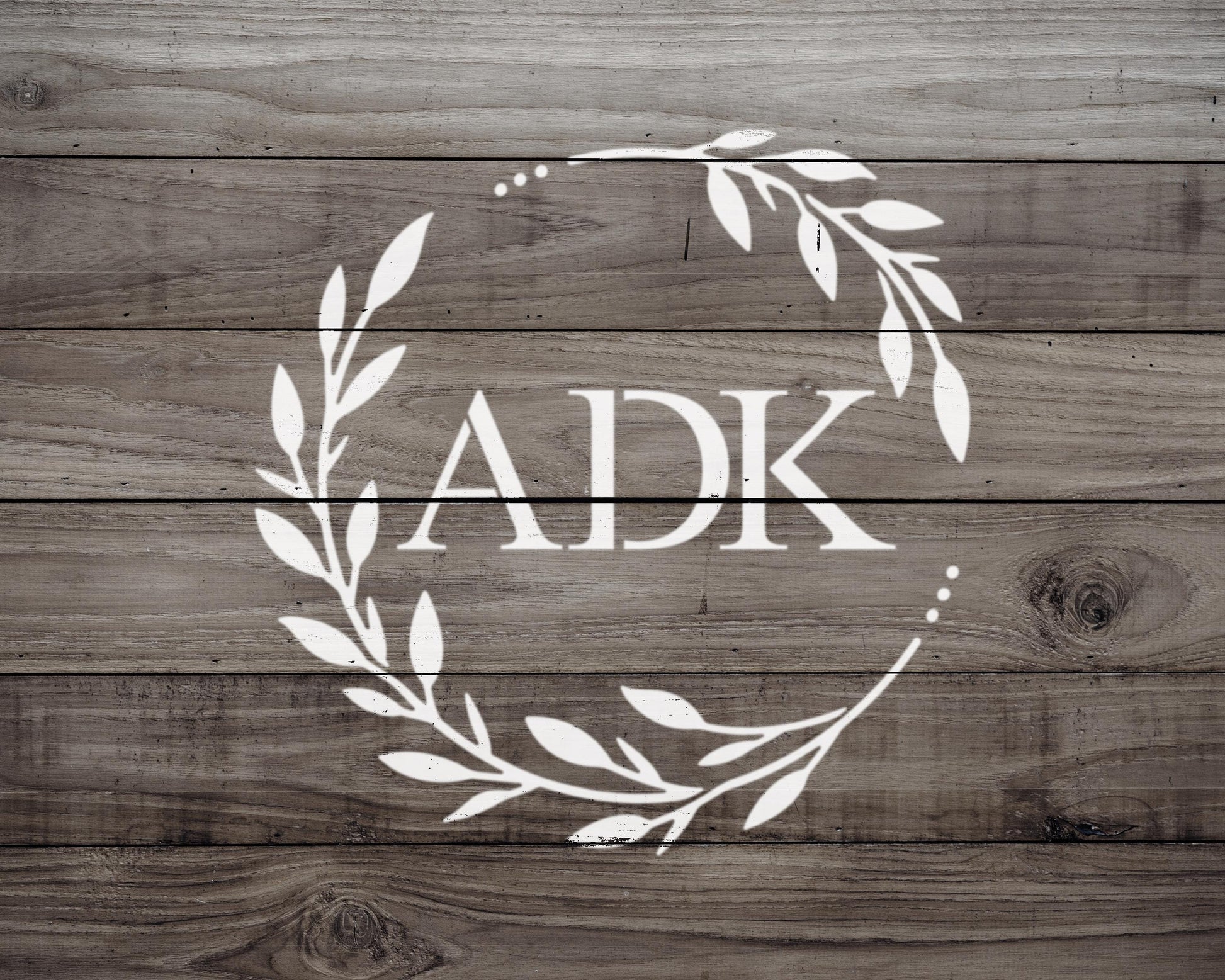 a monogrammed logo with the letters "AK" in the center, surrounded by a wreath-like design made up of leaves and branches.